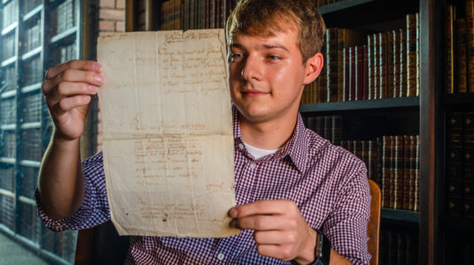 Dillon Prus holds historic Belgian letter found in the Clark University archives.