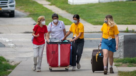 orientation leaders help students with red moving bin move onto campus