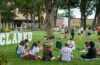 students sit in circle on campus green next to #CLARKU letter