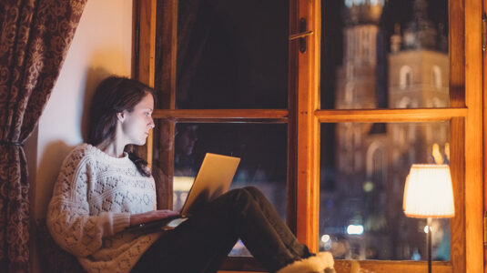 Woman sitting in large window using a laptop