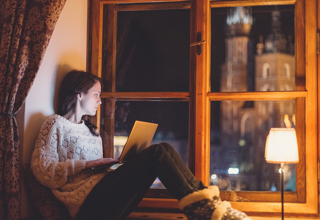 Woman sitting in large window using a laptop