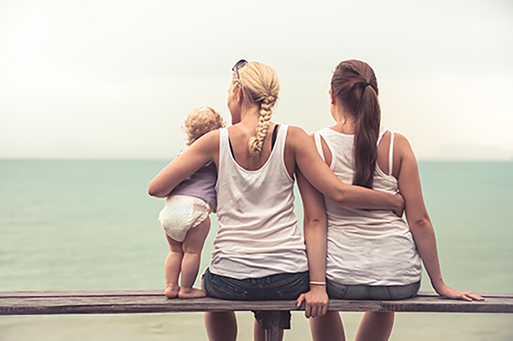 Two mothers with child looking out at ocean