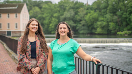 Stephanie Covino, M.S. ’15 (r.), manager of the Blackstone Watershed Collaborative, and Caleigh McLaren ’22, M.S. ’23, restoration coordinator for the Collaborative, at the Slater Mill Dam.