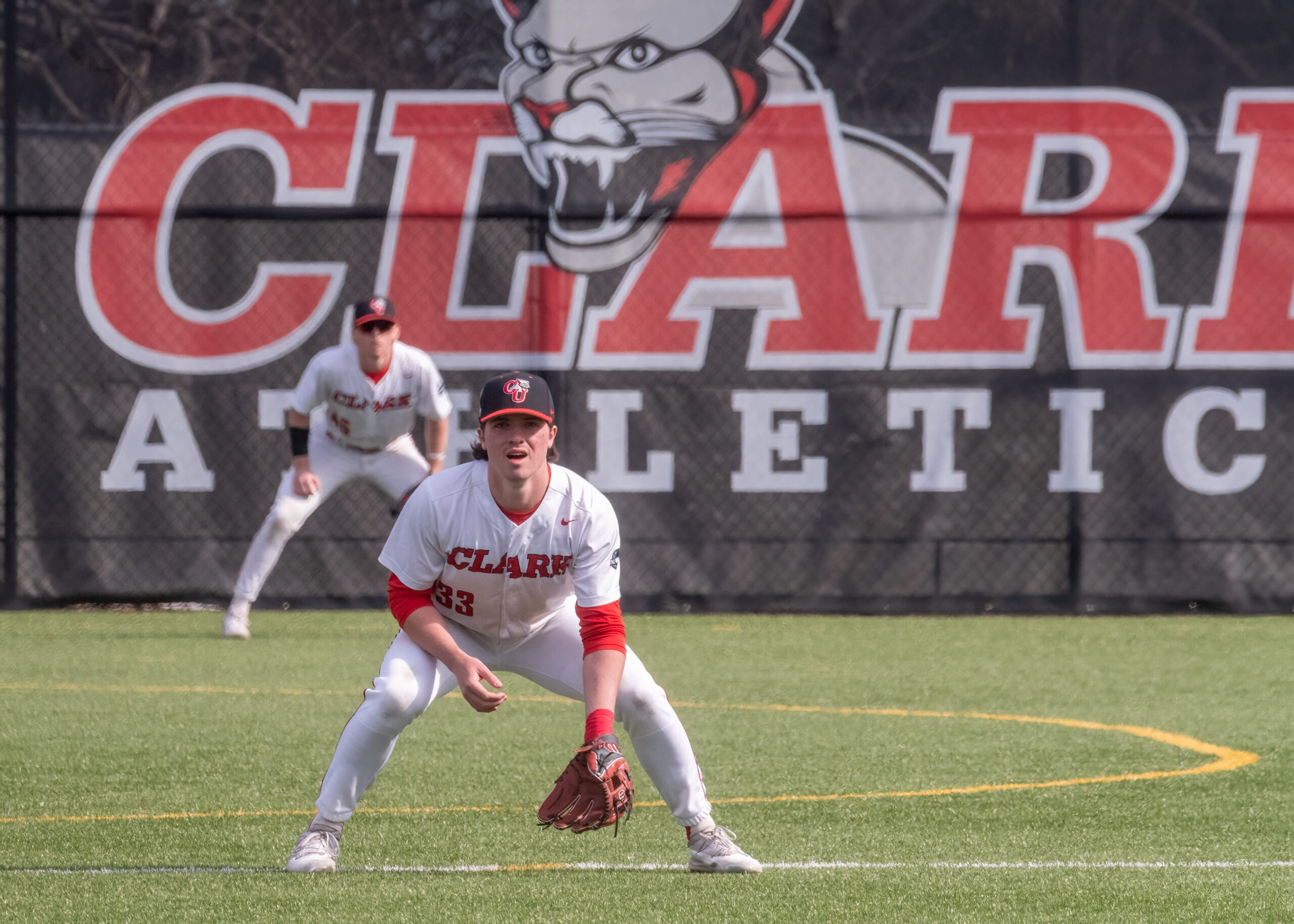 Baseball players in front of Clark Athletics sign.