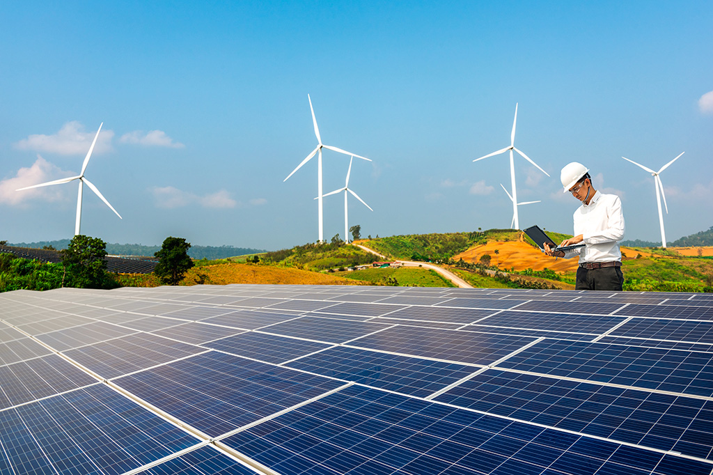 Worker uses laptop to monitor solar energy array, wind turbines