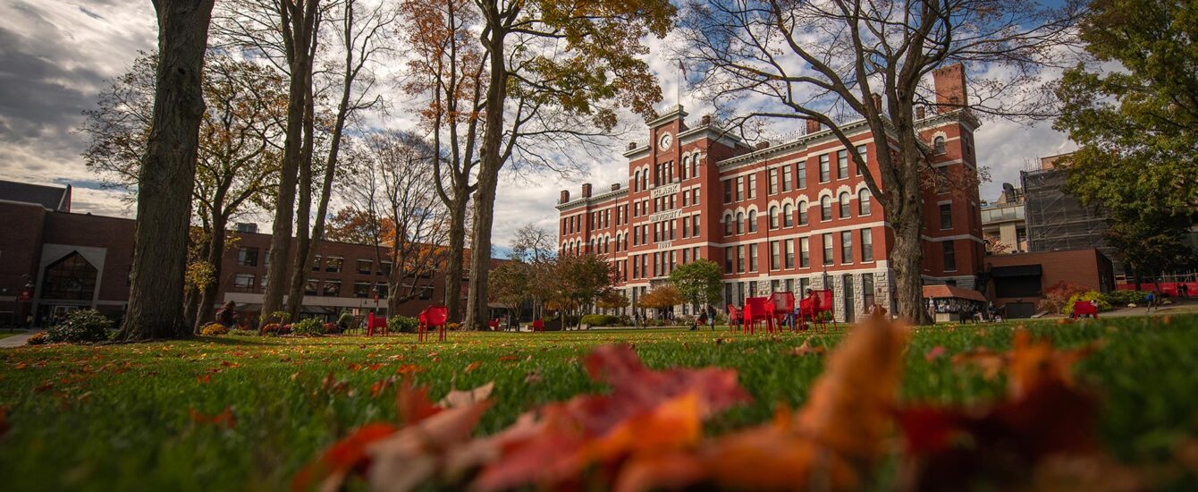 A close-up of fall leaves on grass in the foreground with Jonas Clark Hall in the distance