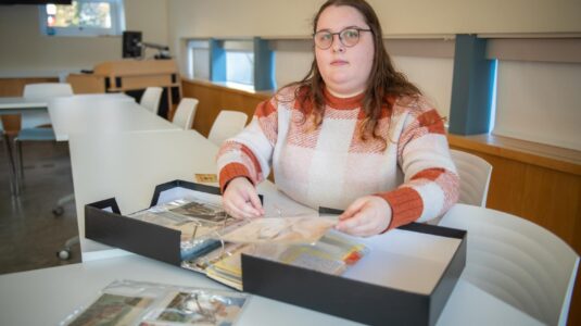 student flips through binder of postcards