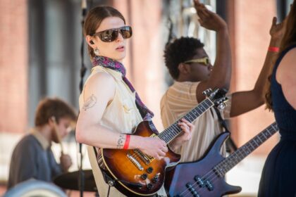 student wearing sunglasses plays guitar on stage