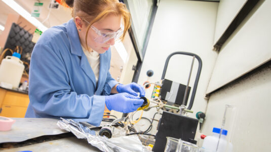 student wearing blue works in lab