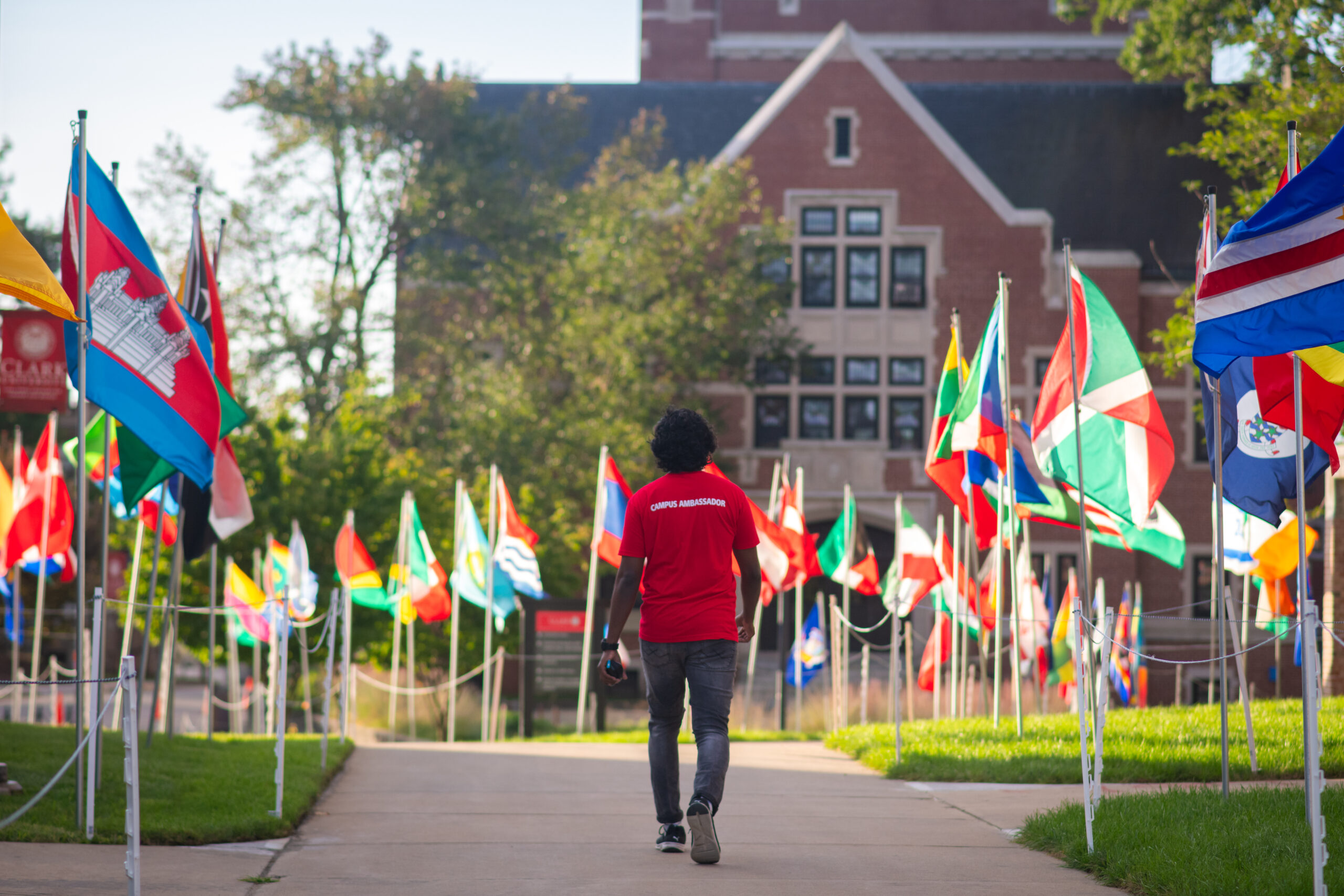 student in red T-shirt walking on path with flags