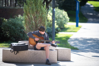 student sitting down playing acoustic guitar