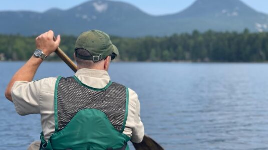 man padding canoe on lake surrounded by mountains