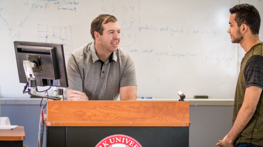 man at computer talking to student