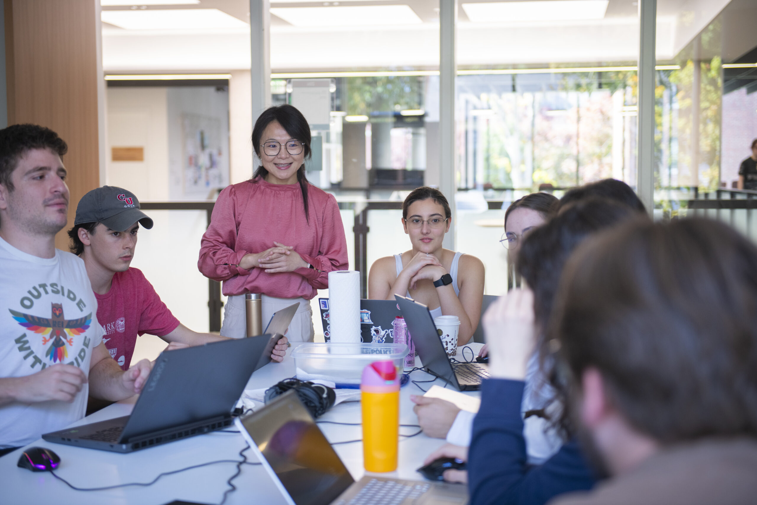 professor talks to students seated at table