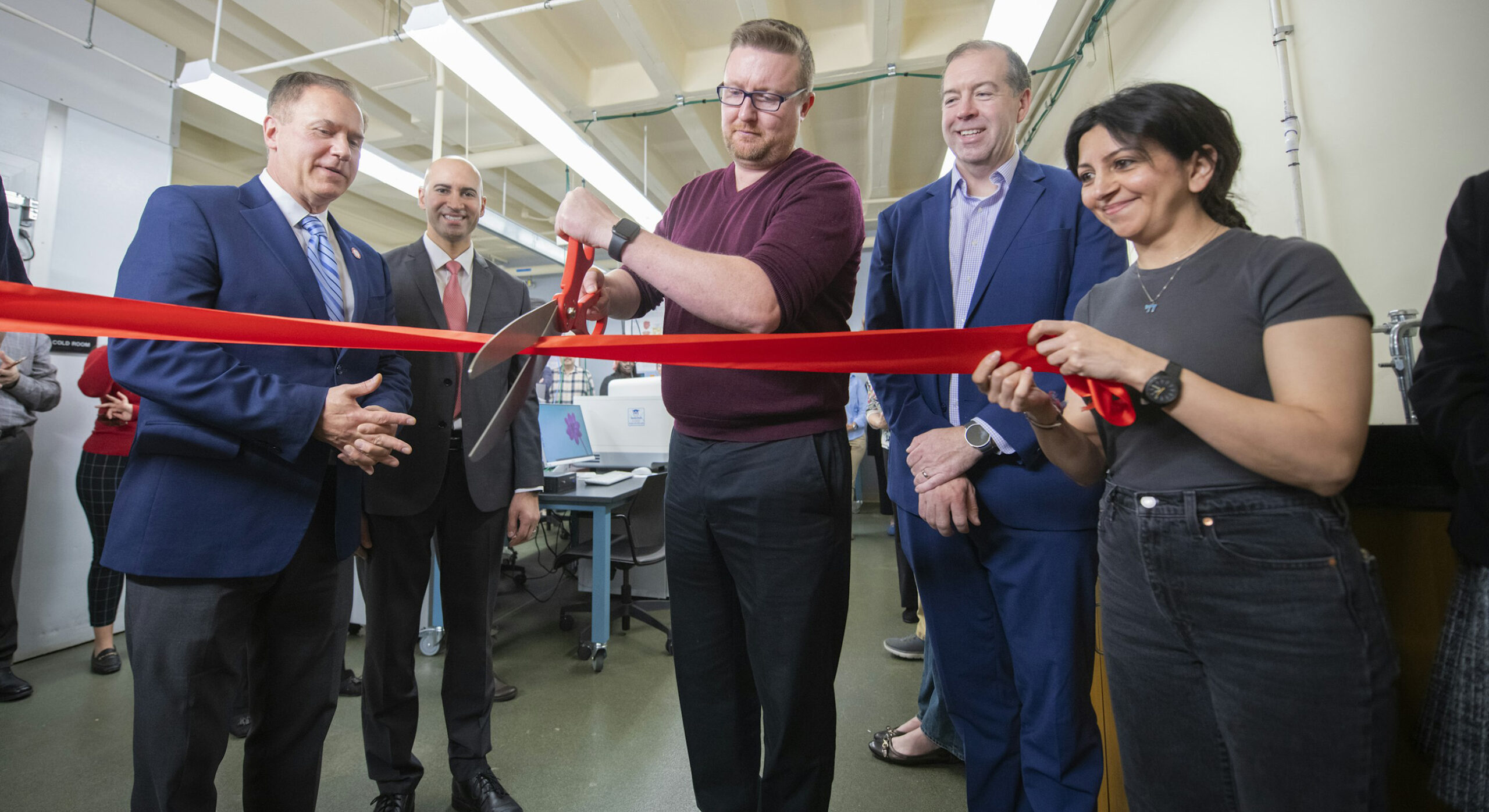 Don Spratt cuts the red ribbon at the lab opening as people look on