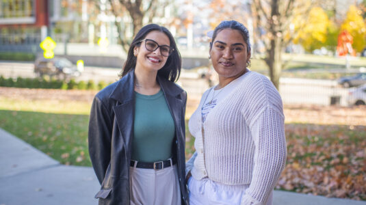 two students pose for photo on campus green