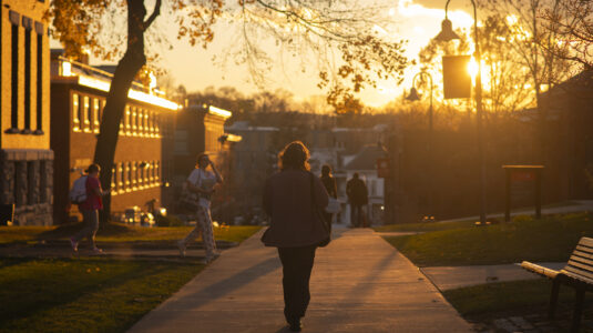 Clark student walking behind Jonas Clark Hall at sunset