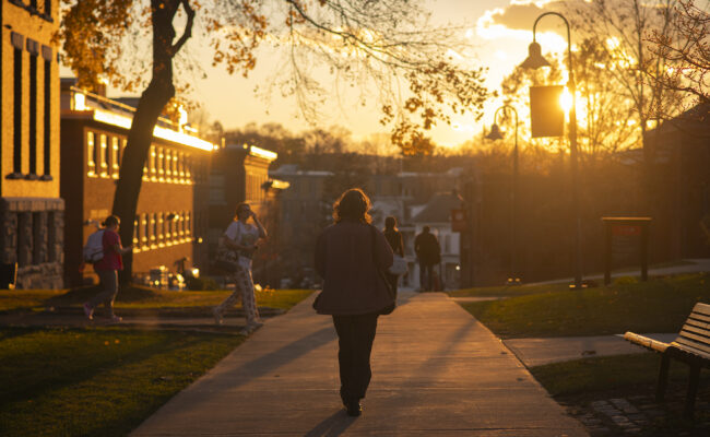 Clark student walking behind Jonas Clark Hall at sunset