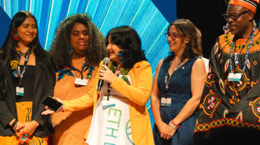 At the XPRIZE Rainforest awards ceremony in Rio de Janeiro, Marina Gatto, an Indigenous scientist from Aldeia Inhãa-Bé and a member of Team ETH BiodivX speaks on behalf of the team, which won the $250,000 Bonus Prize. From left are Kim Puremana, a representative from Aldeia Inhãa-Bé; Kamila Camilo, a team member from Instituto Oyá; Clark Geography Professor Florencia Sangermano, the only U.S. team member; and Kevin Njavo, one of several judges for the competition.