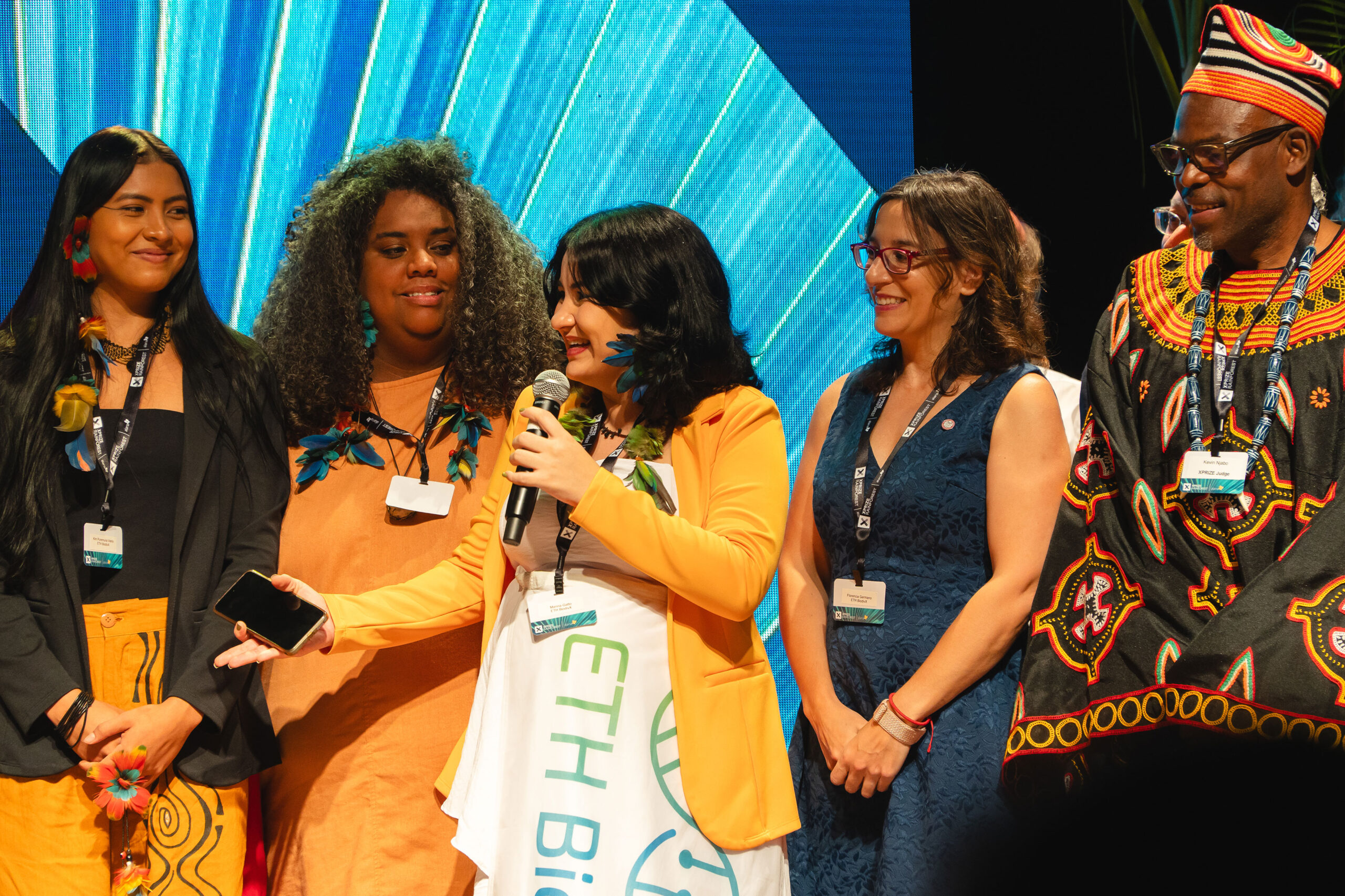 At the XPRIZE Rainforest awards ceremony in Rio de Janeiro, Marina Gatto, an Indigenous scientist from Aldeia Inhãa-Bé and a member of Team ETH BiodivX speaks on behalf of the team, which won the $250,000 Bonus Prize. From left are Kim Puremana, a representative from Aldeia Inhãa-Bé; Kamila Camilo, a team member from Instituto Oyá; Clark Geography Professor Florencia Sangermano, the only U.S. team member; and Kevin Njavo, one of several judges for the competition.