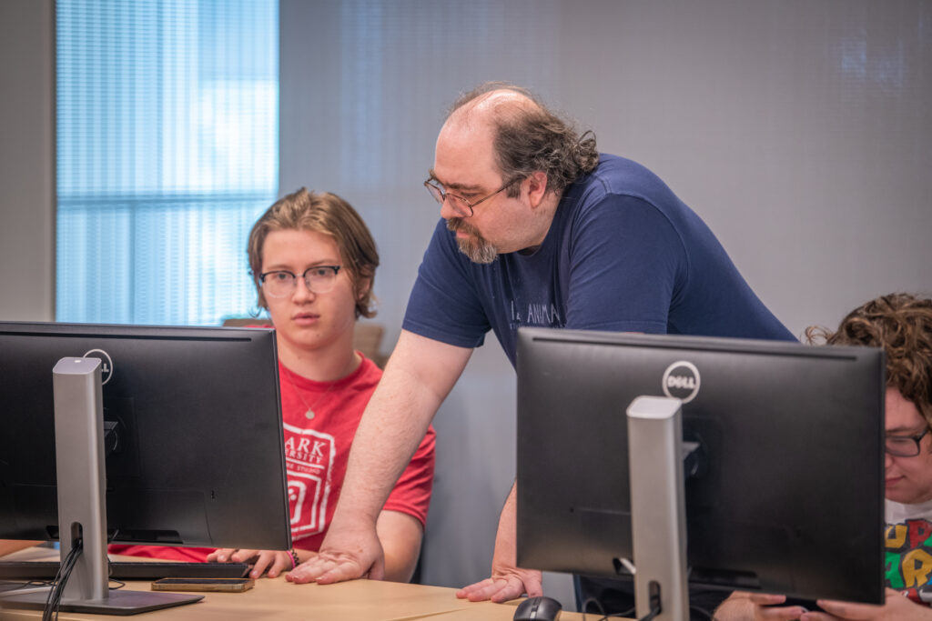 professor guides student at computer