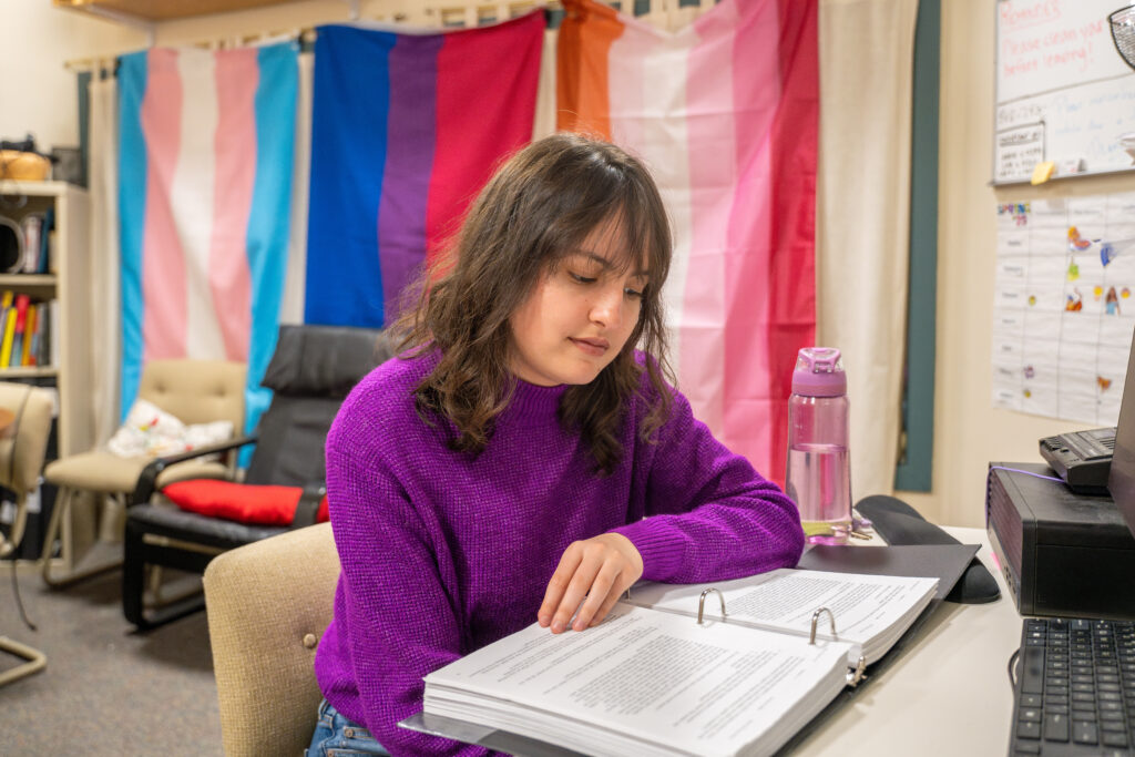 student reads documents with pride flags in background